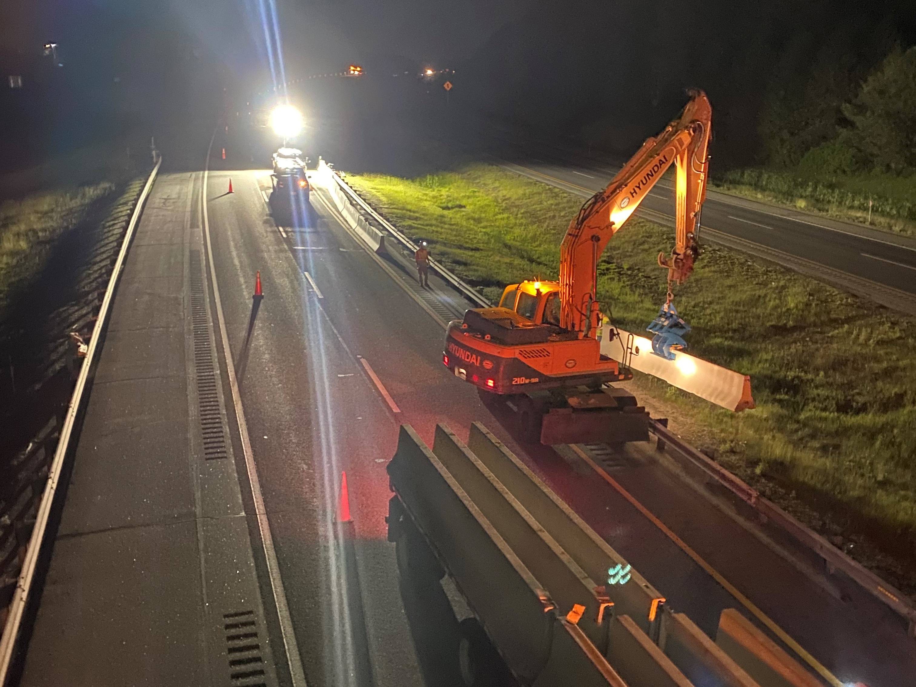 Cranes at night lifting temporary barricade pieces into postion on the highway.